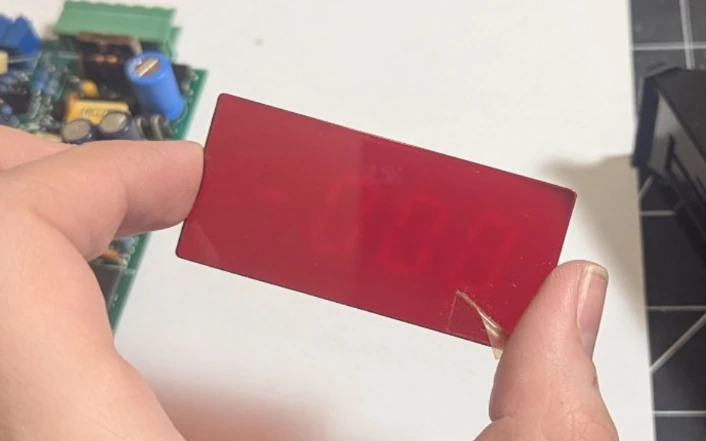 A dark red tinted piece of glass is held above a white piece of paper, and certain areas corresponding to the segments of the LED digits can be seen burned in.