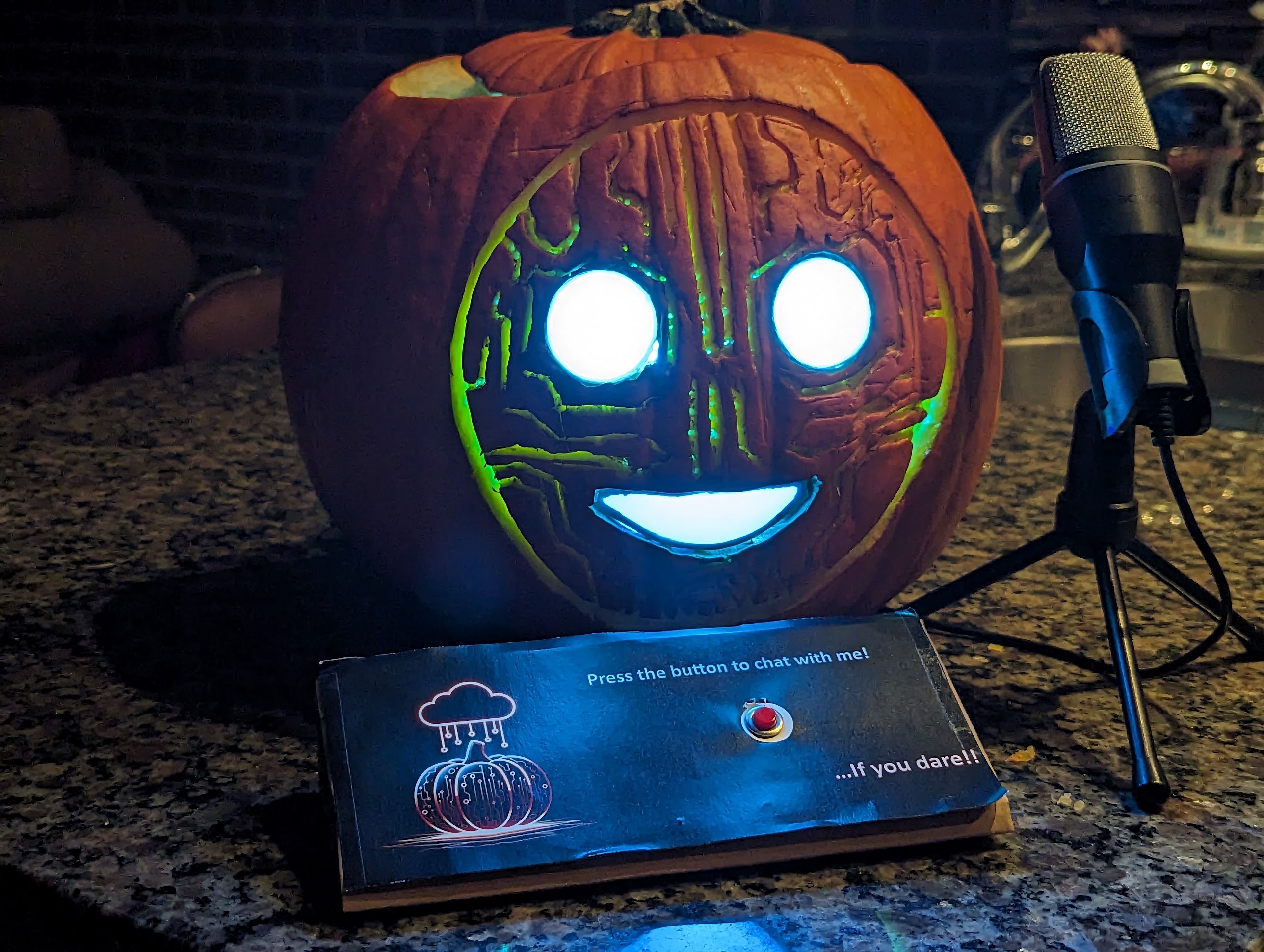 A picture of a jackolantern with an artificial looking smile. circuit traces are carved it is face. Its blank eyes and mouth glow blue. In front of it sits a button panel that says 'Press the button to chat with me... if you dare!