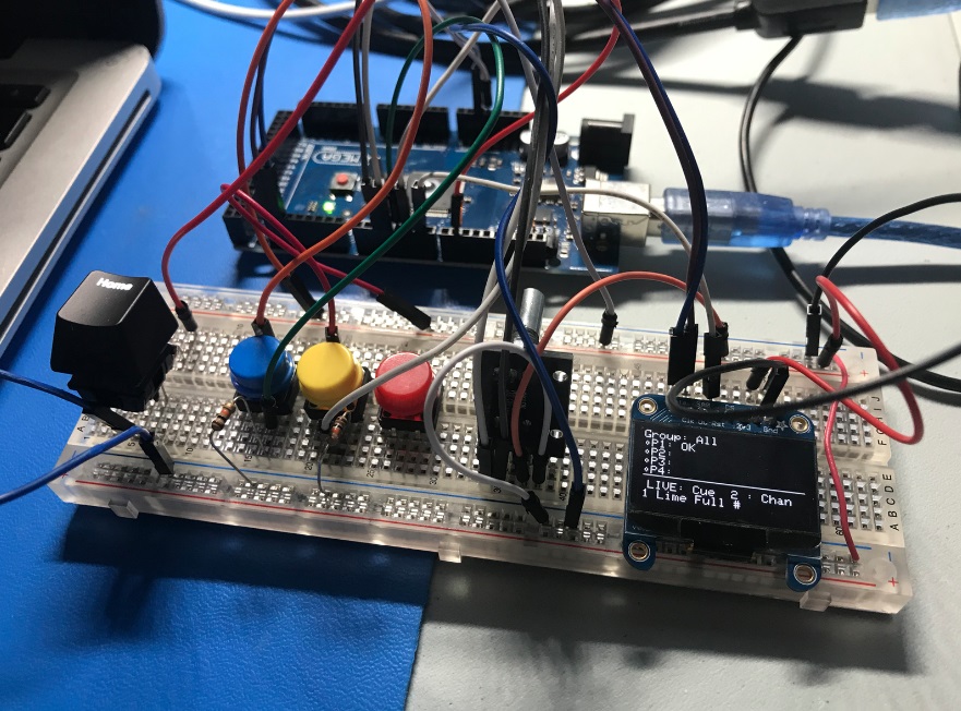An electronics prototyping breadboard with multiple buttons, an encoder, and a screen showing lighting information.